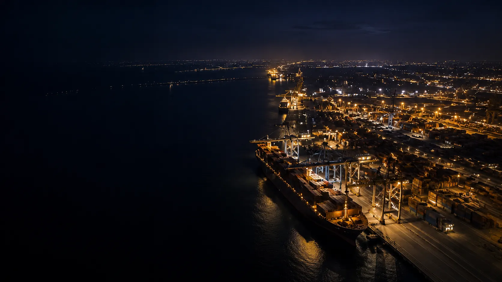 Aerial night view of a cargo terminal with container operations and port lighting.